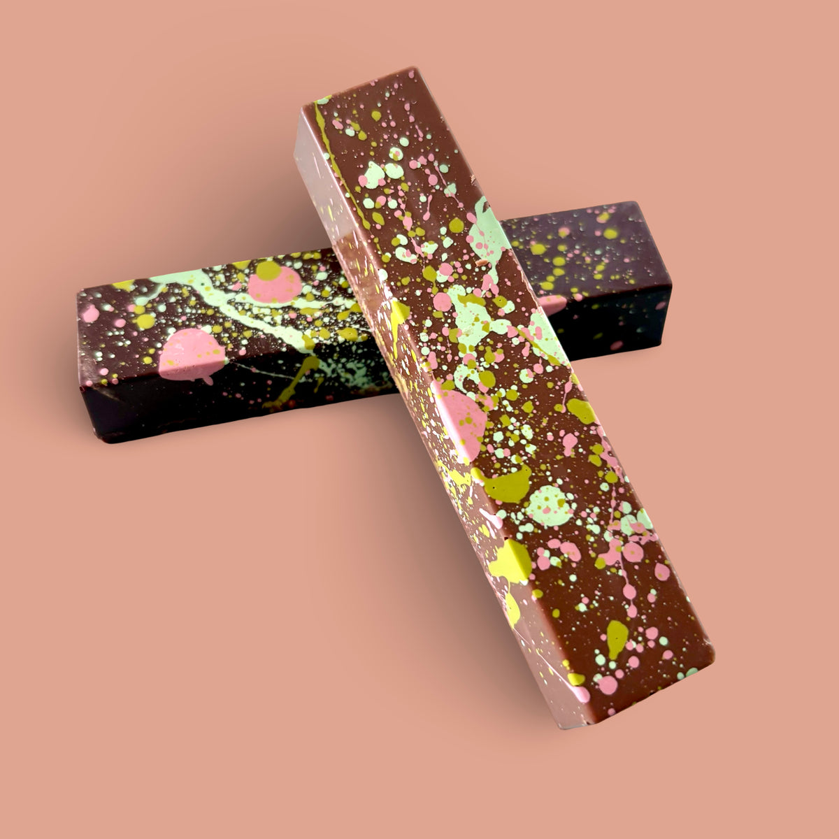 Two Poppy & Peep Dubai chocolate bars with colorful paint splatters