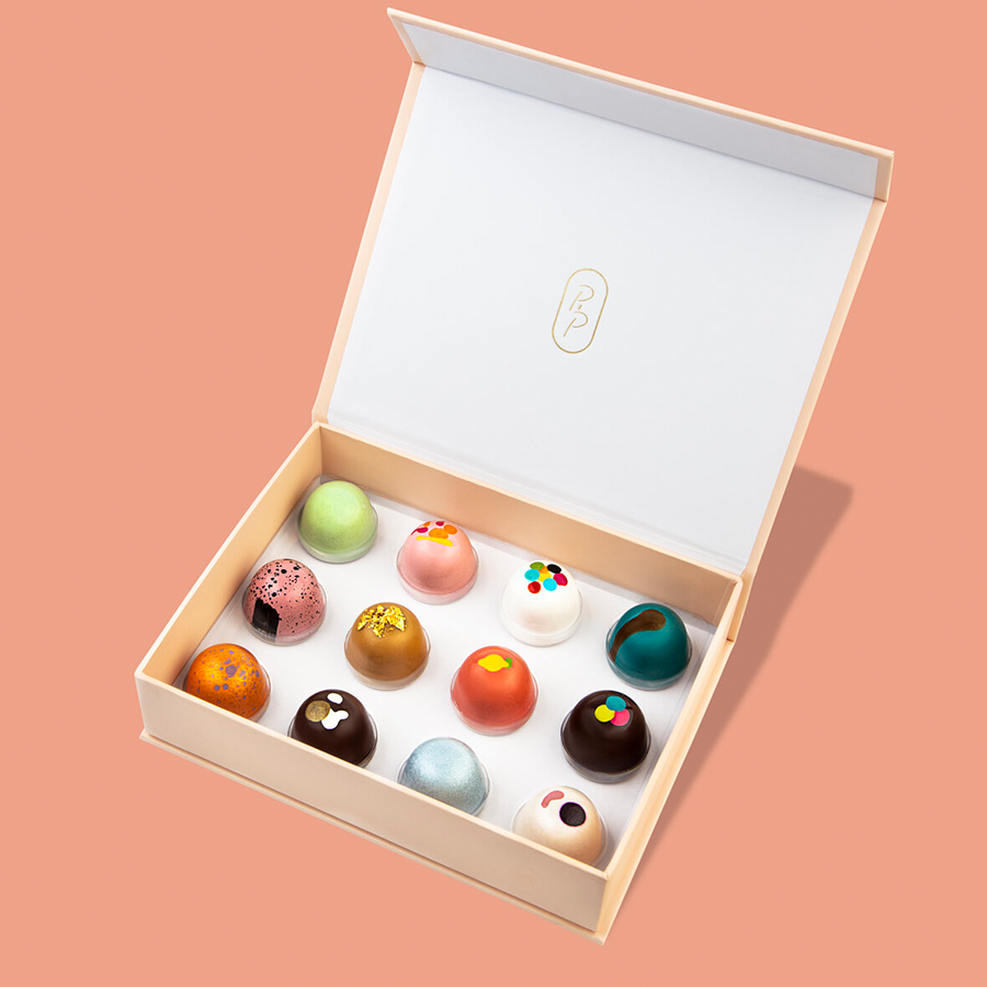 A box of assorted handcrafted bonbons in an open box, with a variety of colors and flavors represented.